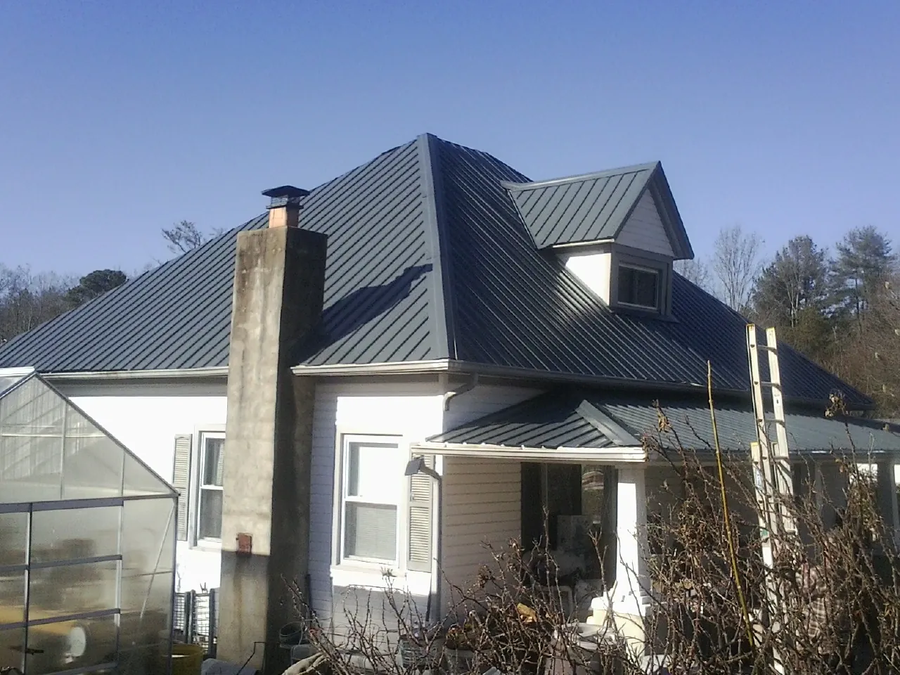 Dark blue standing seam metal roof on a white farmhouse with dormer — Slate & Tile Roof Repair by Roofing Brothers in South Mills