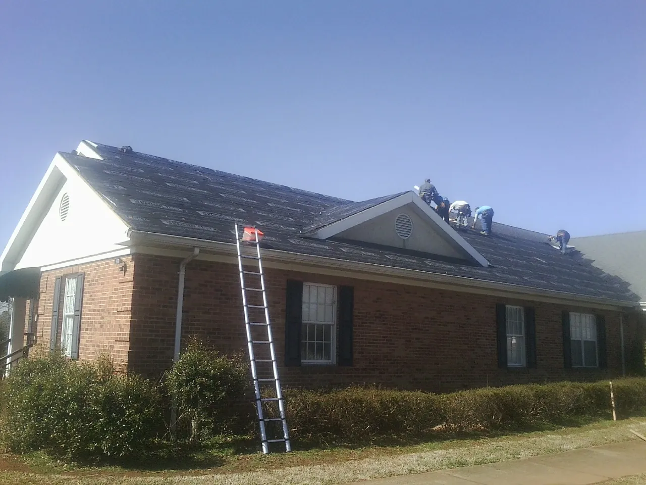 Crew tearing shingles off a brick ranch roof with a ladder set — Emergency Roof Repair work by our crew in South Mills