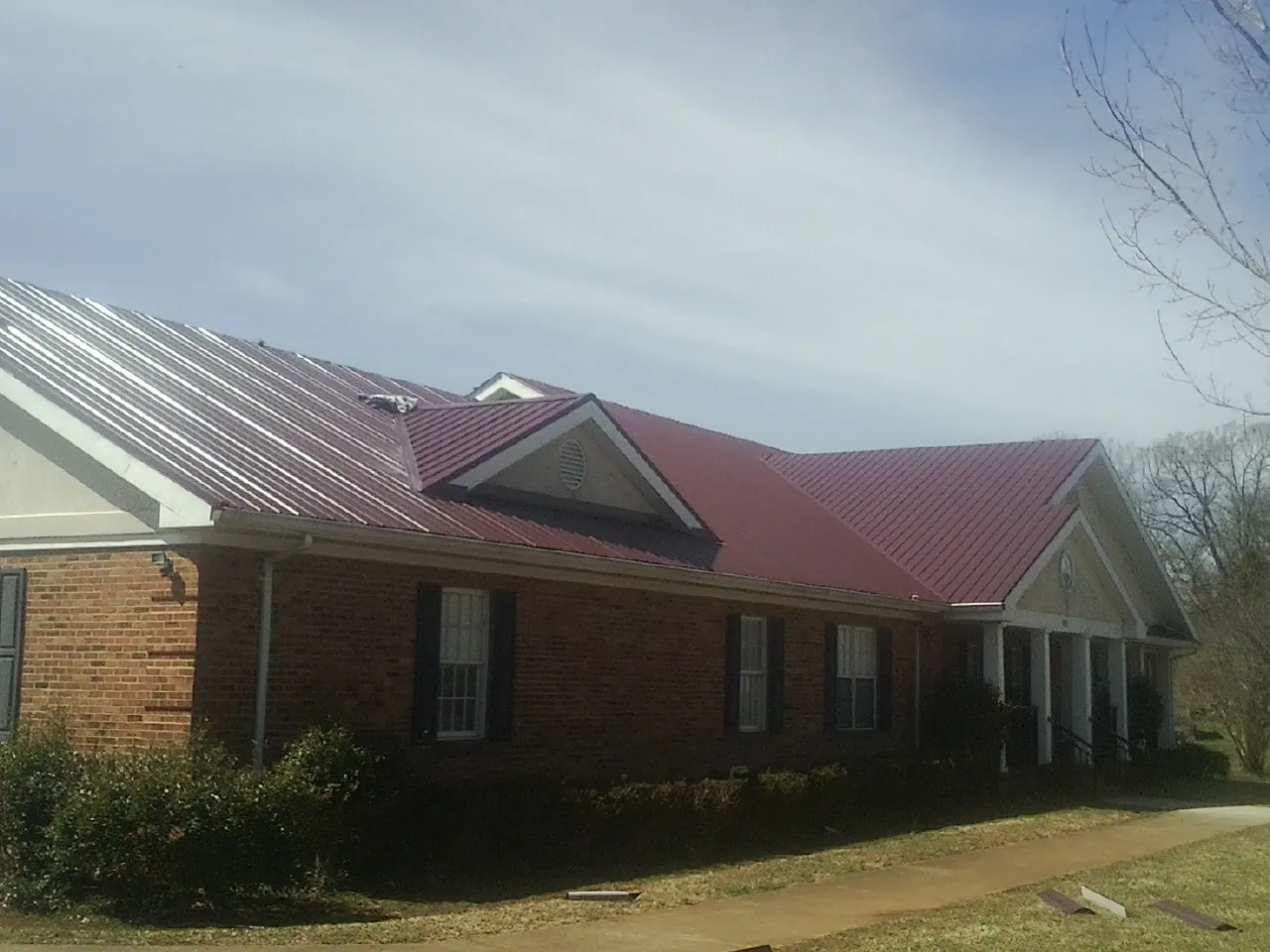 Red metal roof with gabled entries on a long brick building, from a Hail Damage Roof Repair job in South Mills