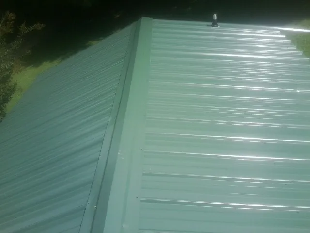New green metal panels meeting at the ridge of a roof — Flat Roof Repair work by our crew in South Mills