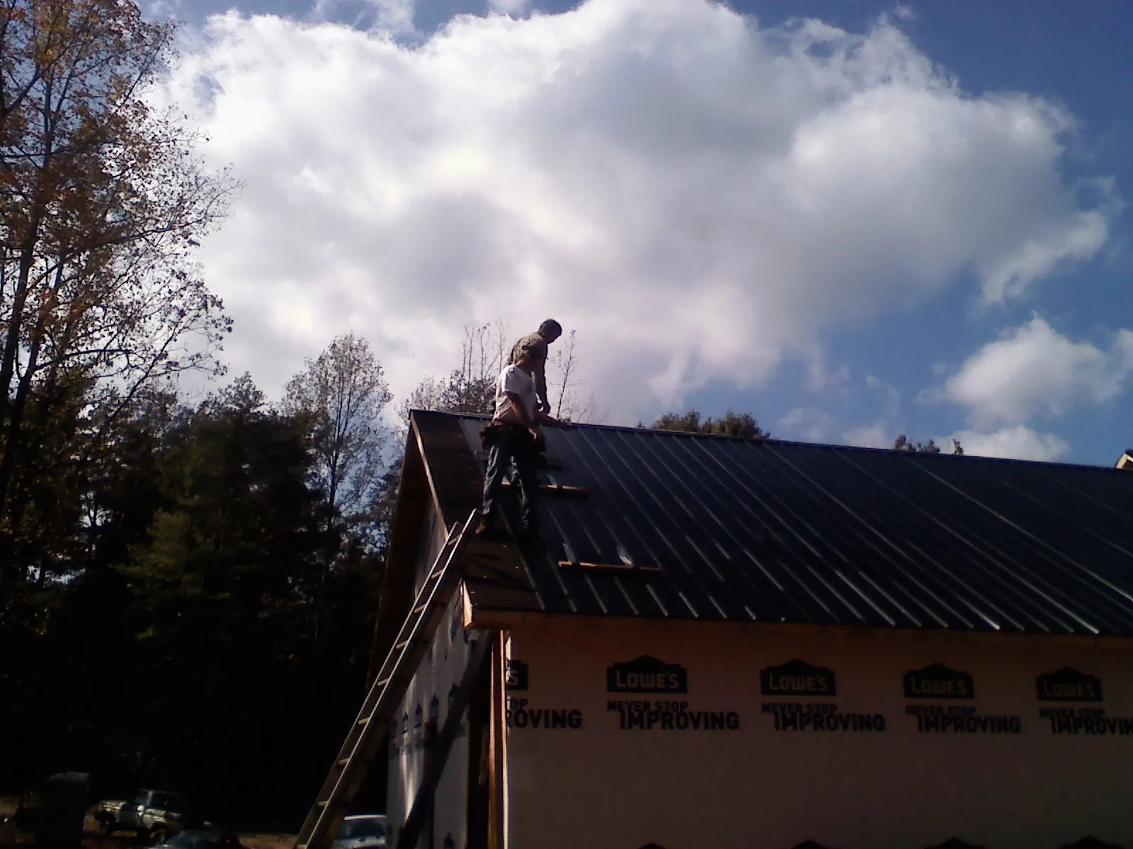 Roofer fastening dark metal panels high against a cloudy sky, from a Roof Inspection job in South Mills