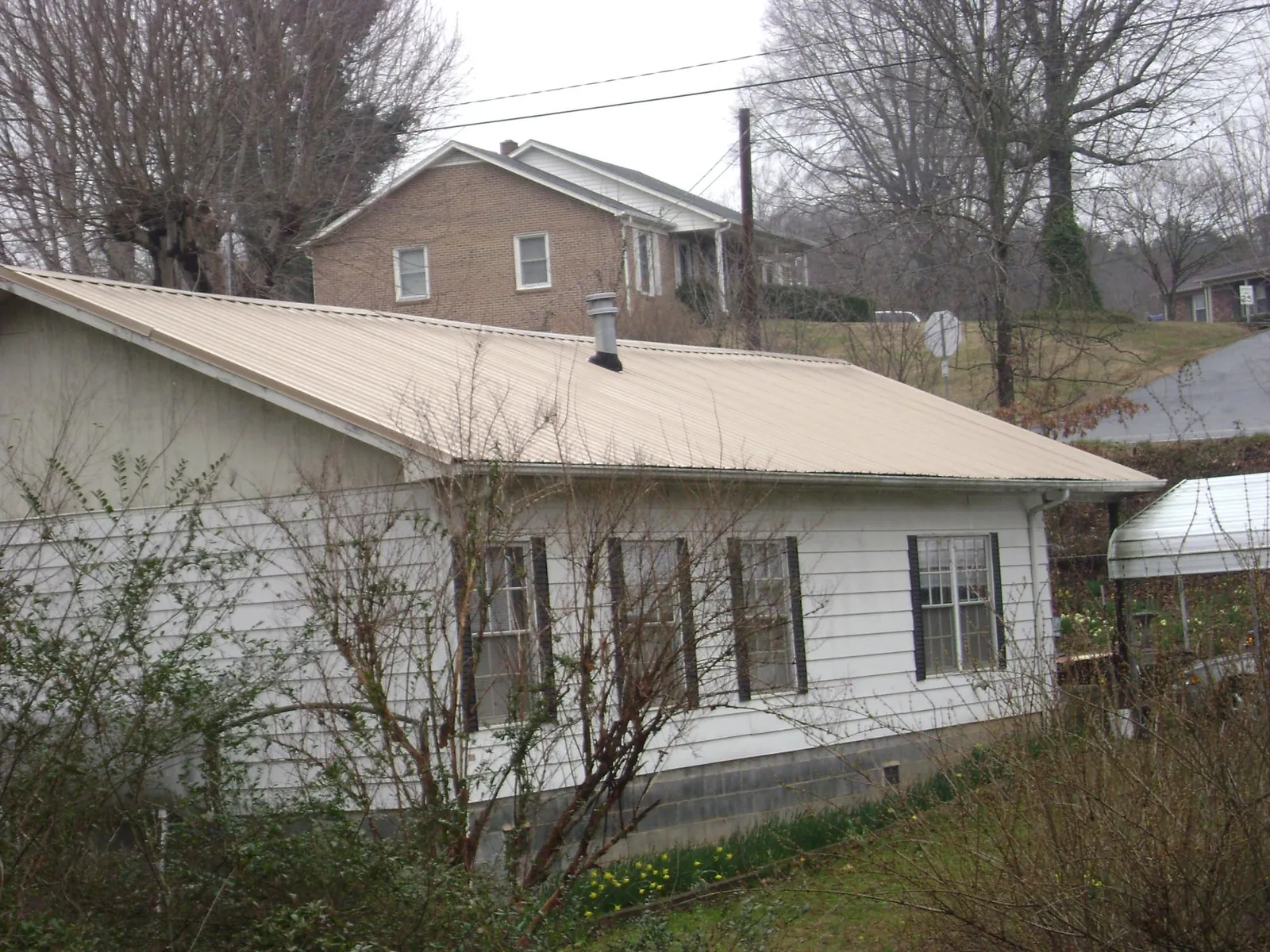 Tan metal roof on a white sided house set into a hillside — Commercial Roofing by Roofing Brothers in South Mills